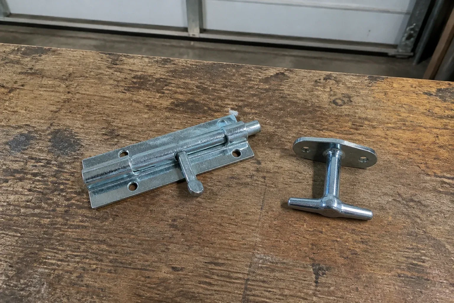Detached slide bolt and T-handle on a wooden garage workbench. — Garage Door Manual Lock Repair, Port Colborne